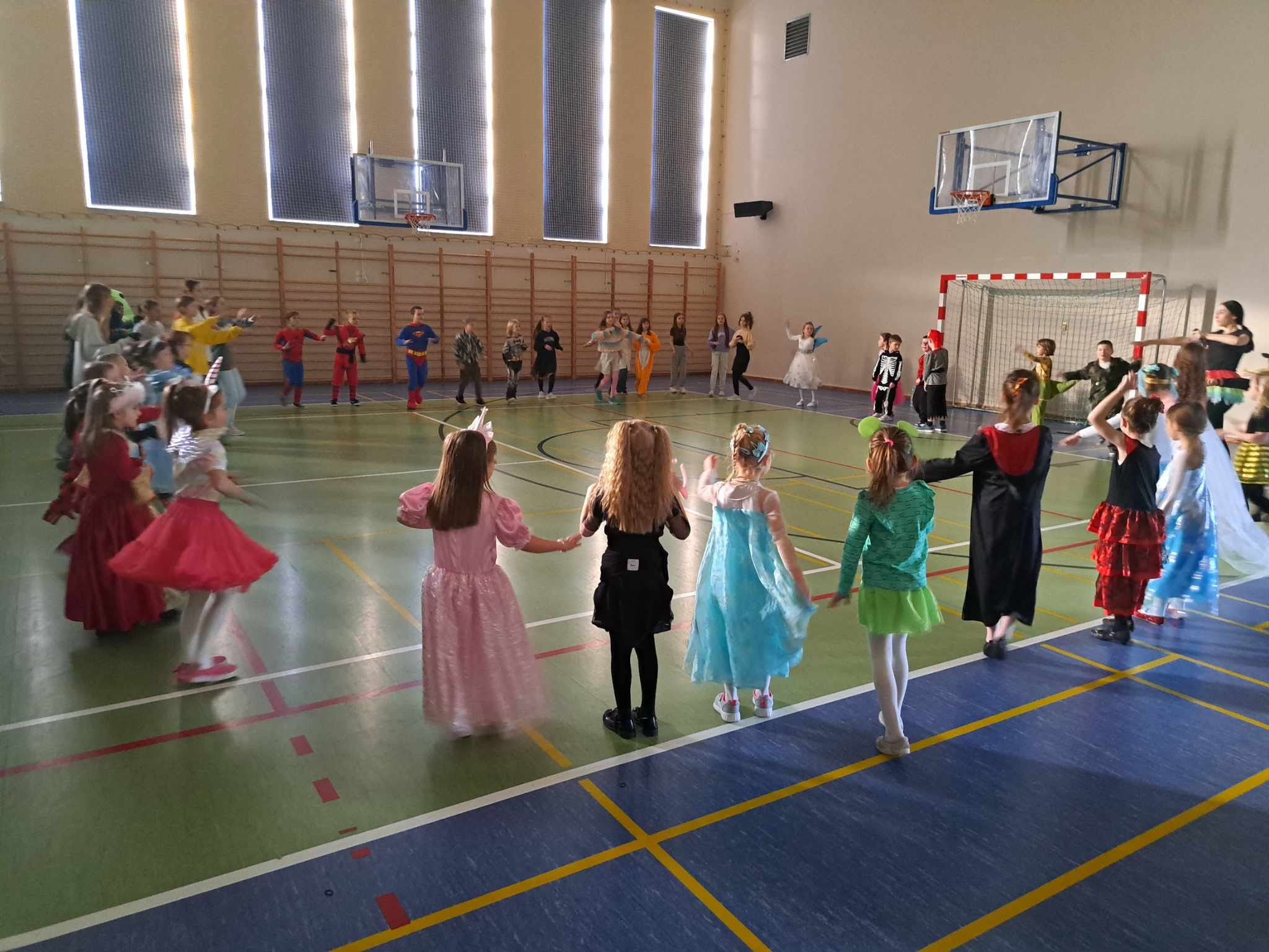 Dzieci w strojach karnawałowych tańczą na sali gimnastycznej