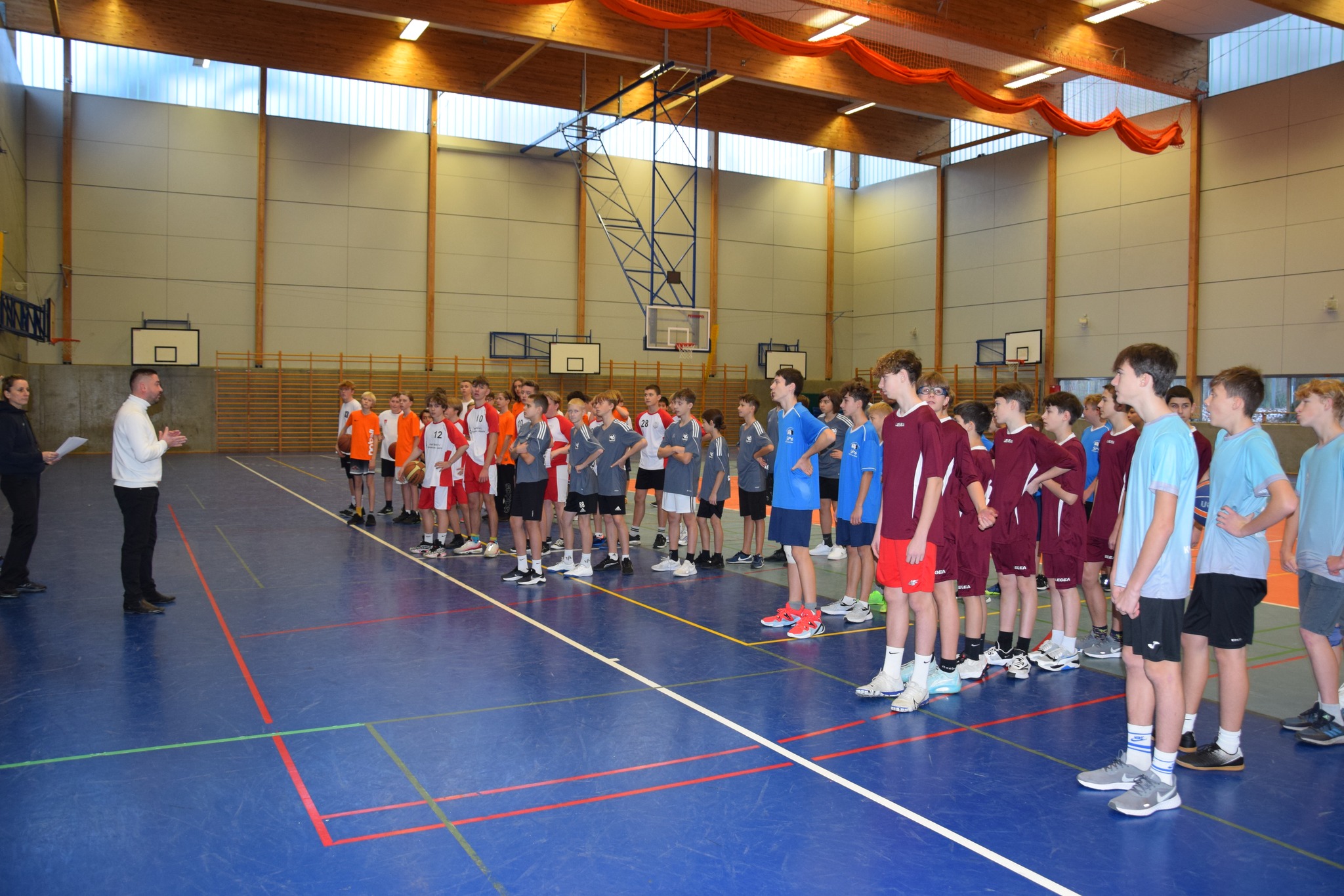 Uczniowie ustawieni drużynami stoją w sali gimnastycznej