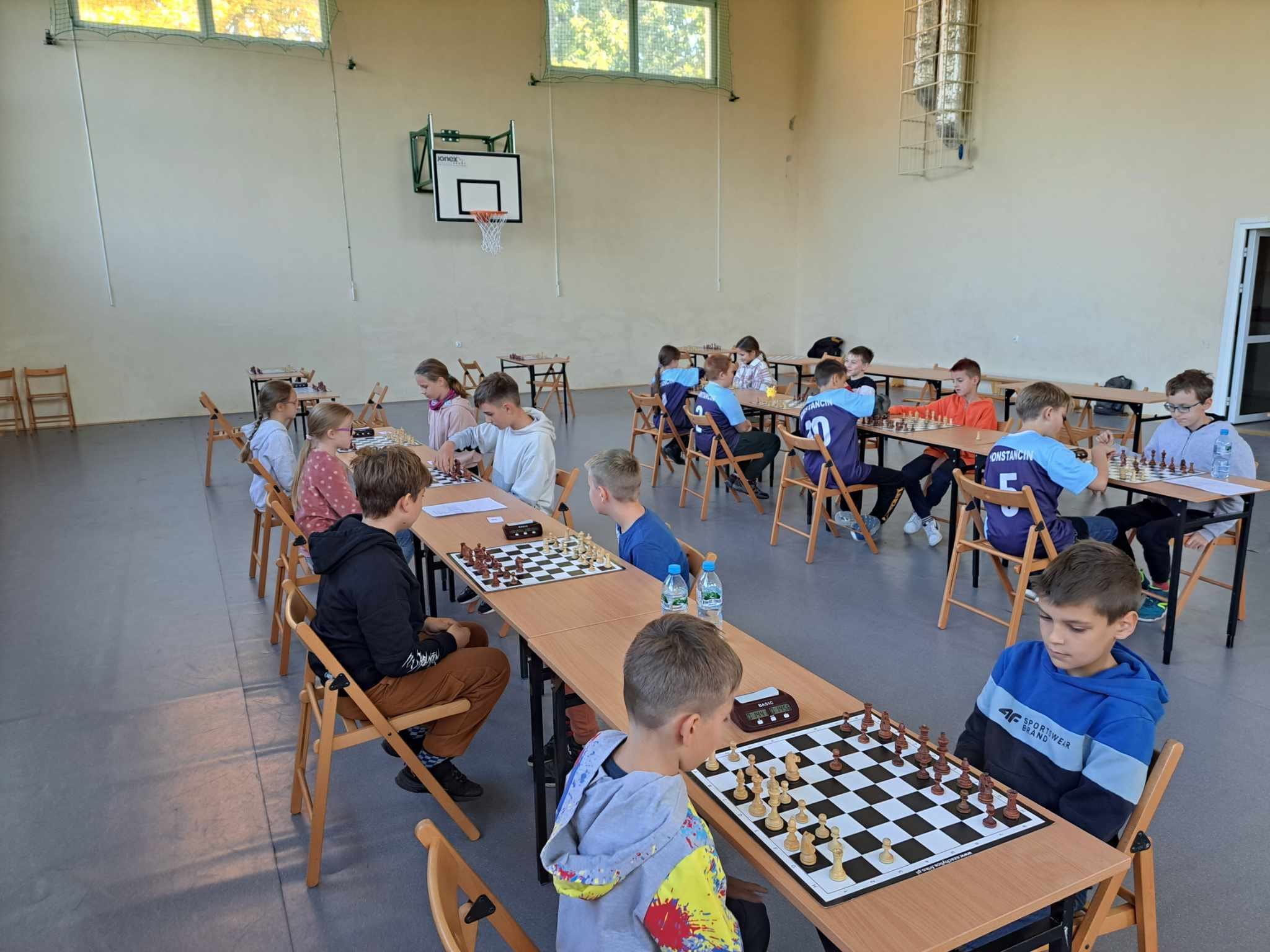 Dzieci siedzą przy stolikach i grają w szachy
